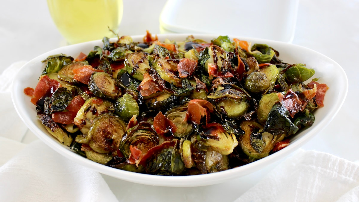 side view of Roasted Balsamic Brussels Sprouts with Prosciutto in a oval white bowl