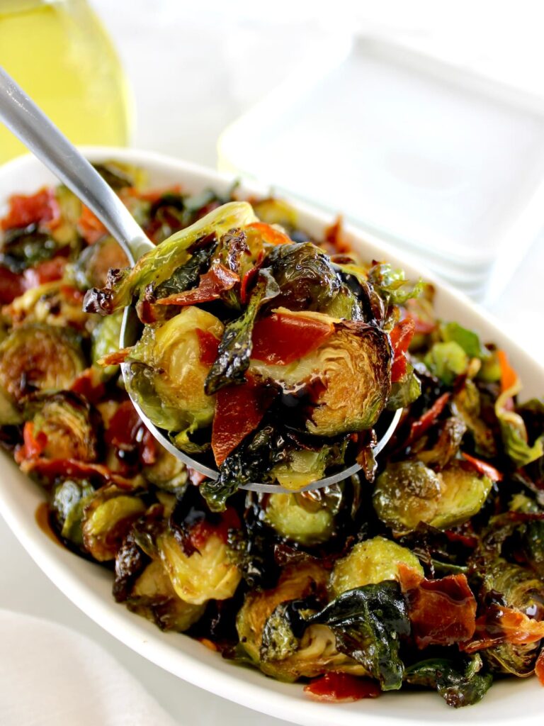 holding up spoonful of Roasted Balsamic Brussels Sprouts with Prosciutto over white bowl