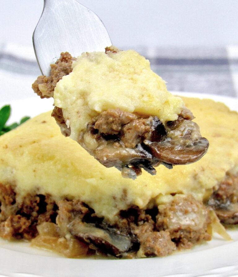 Keto Beef Stroganoff Casserole in fork held up over piece of casserole on white plate